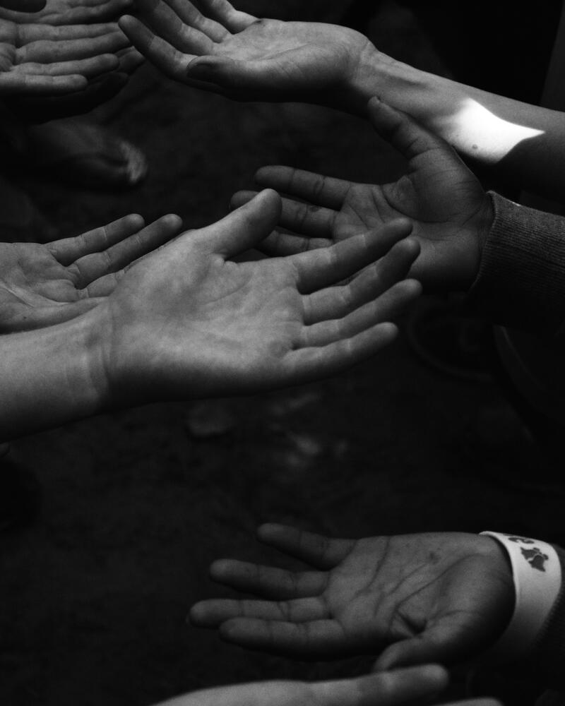 svartvitt foto av flera händer som håller handflatorna mot himlen. 